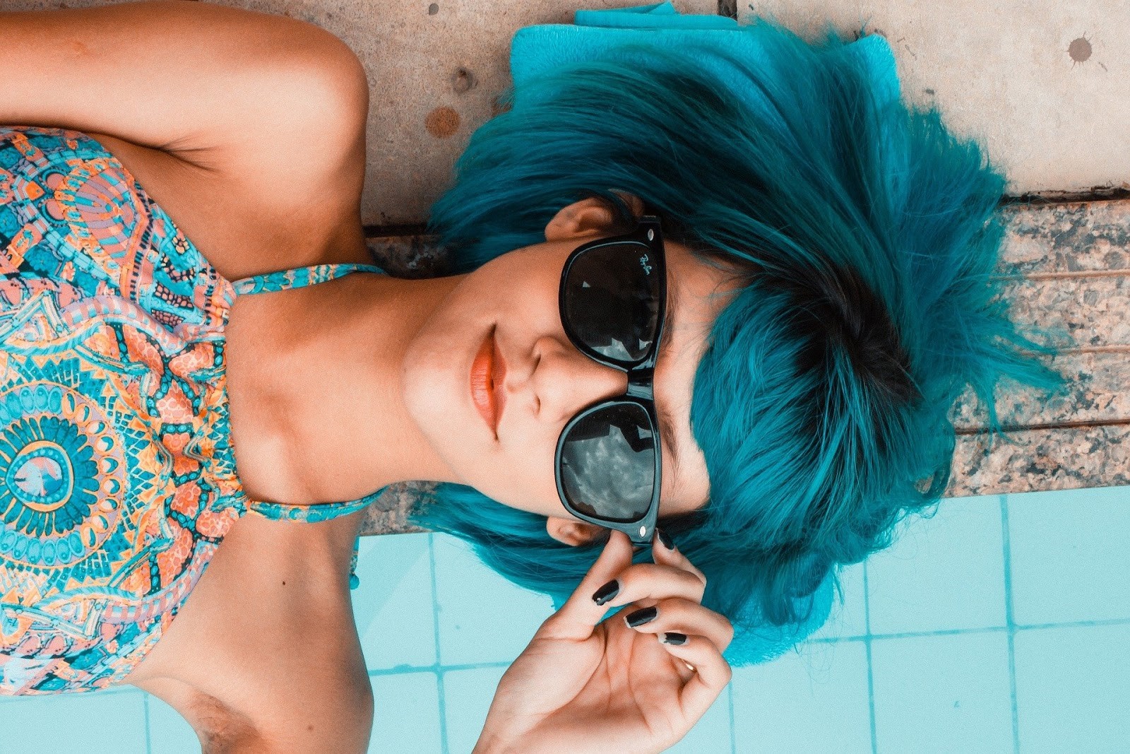 Woman with bluish-green hair wearing sunglasses on a beach